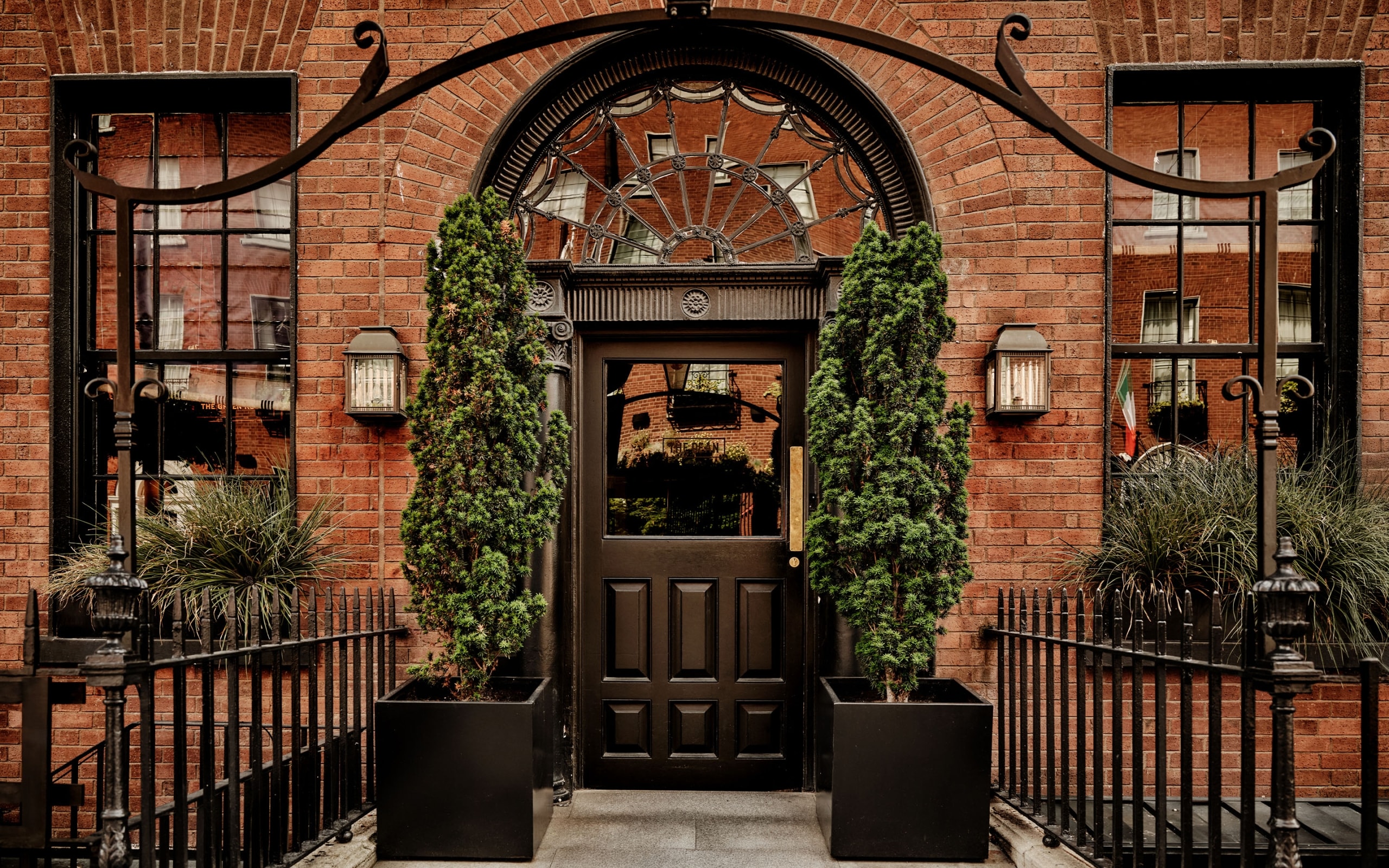 The Entryway of a hotel with two tall trees next to the door