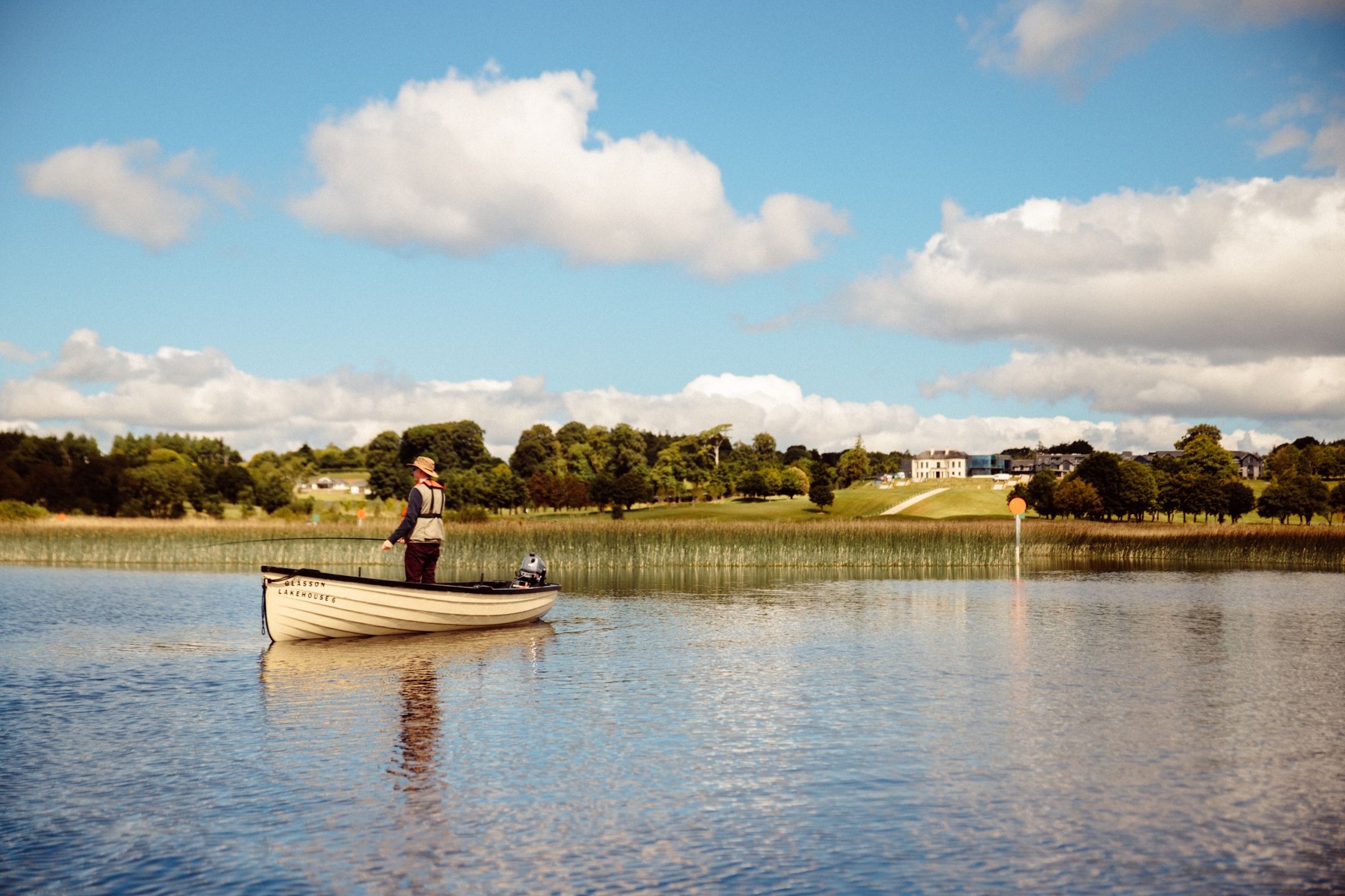 A man fishing on the lake in front of Glasson Lakehouse hotel